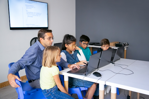 Teacher helping children use laptops